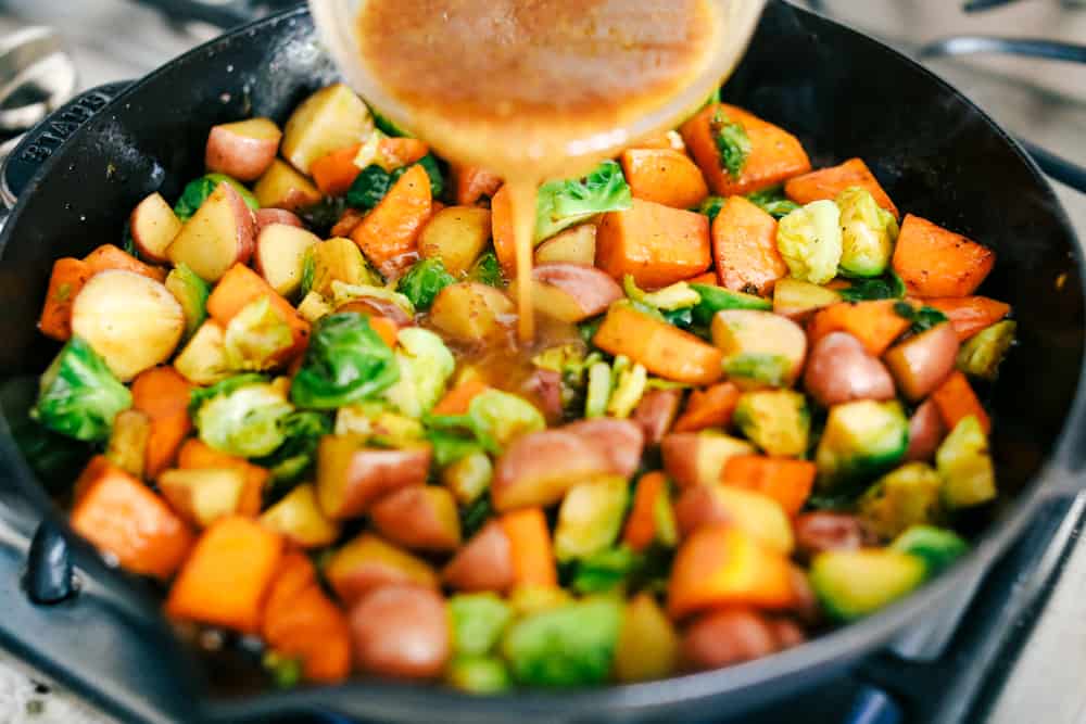 vegetables cooking on the stove top while adding a maple dijon marinate over top of them. 