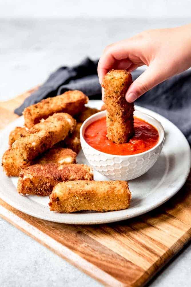 An image of a hand dipping a mozzarella stick into marinara sauce.