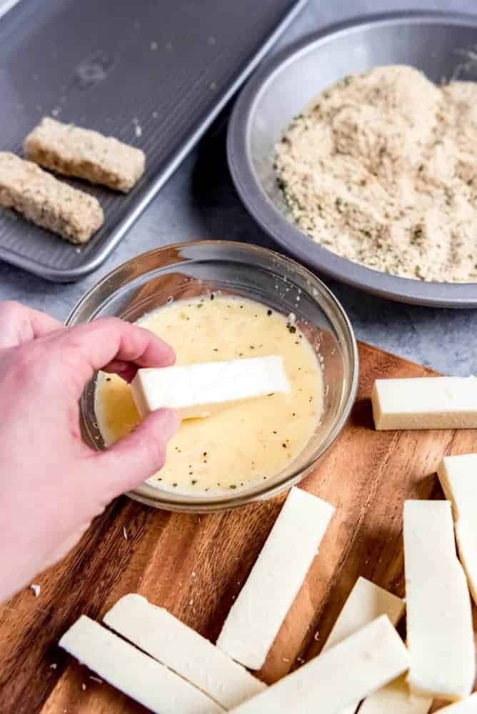 An image of a stick of cheese being dipped in an egg wash bath.