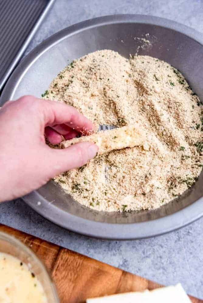 An image of mozzarella cheese being dredged in Italian-seasoned breadcrumbs.