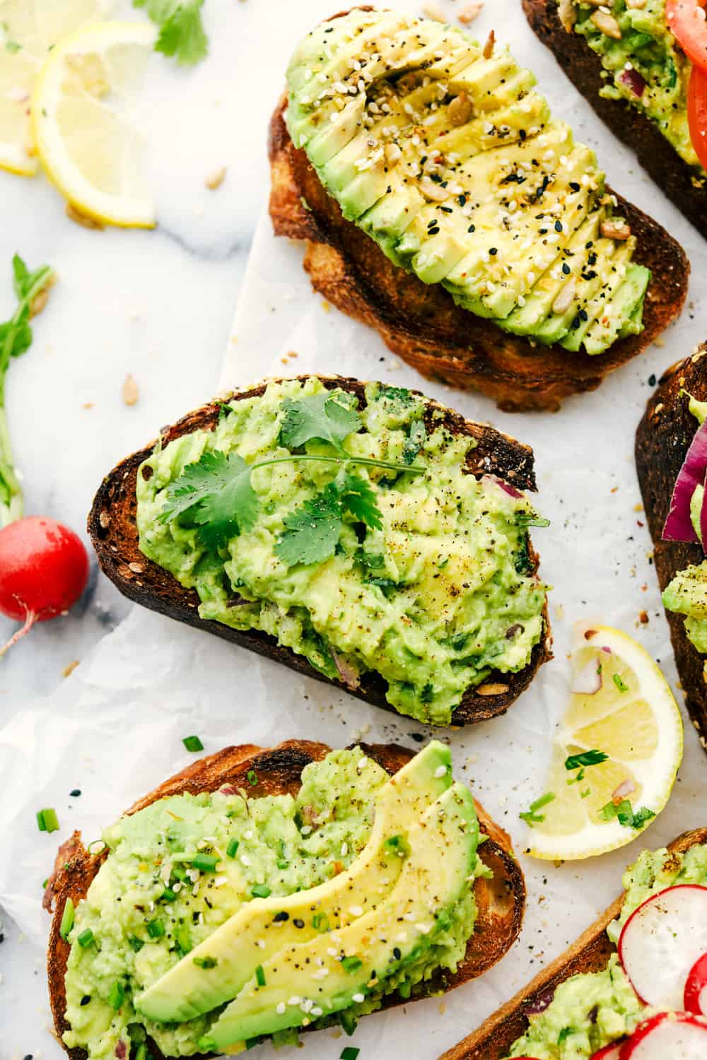 Avocado toast made three different ways with lemon wedges next to them. 