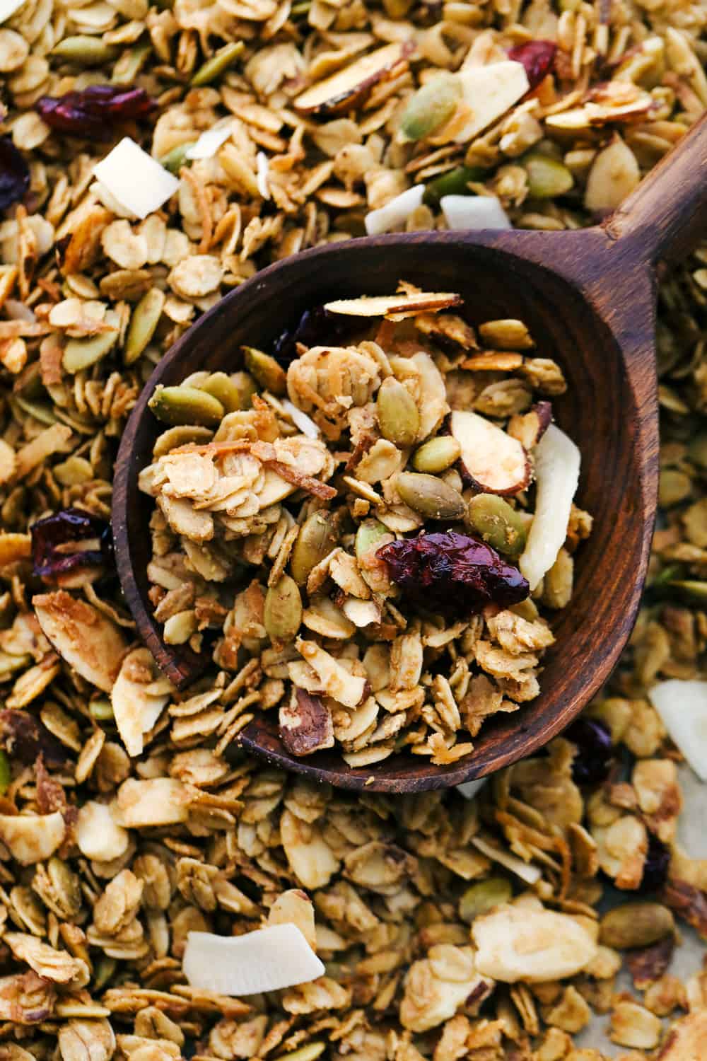 Homemade granola up close photo with it baked on a sheet pan and a wooden spoon. 