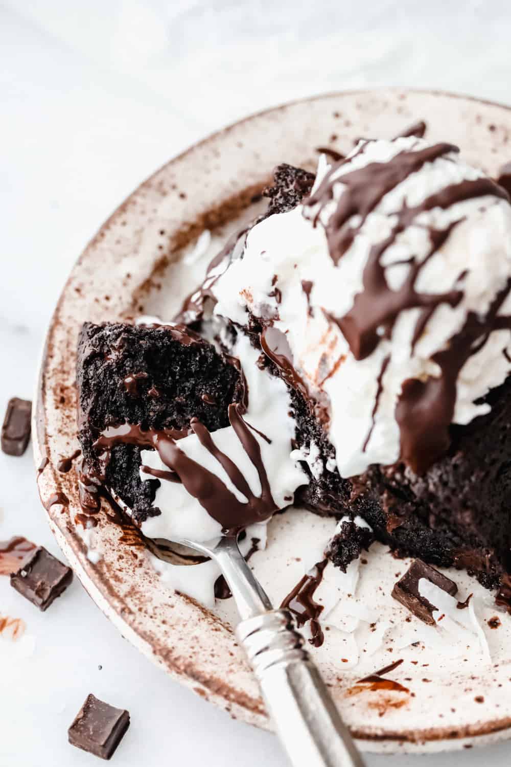 Keto brownie on a plate with a scoop of ice cream with fudge drizzled over top. 