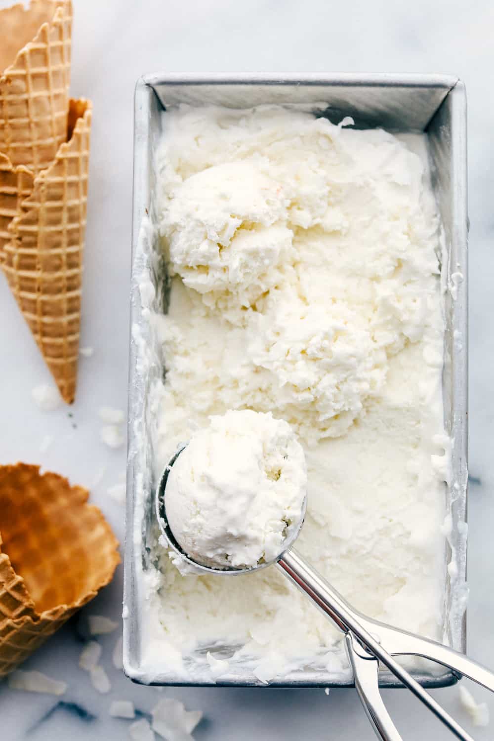 Keto ice cream in a freezer pan with a scoop of ice cream taken out and waffle cones next to it. 