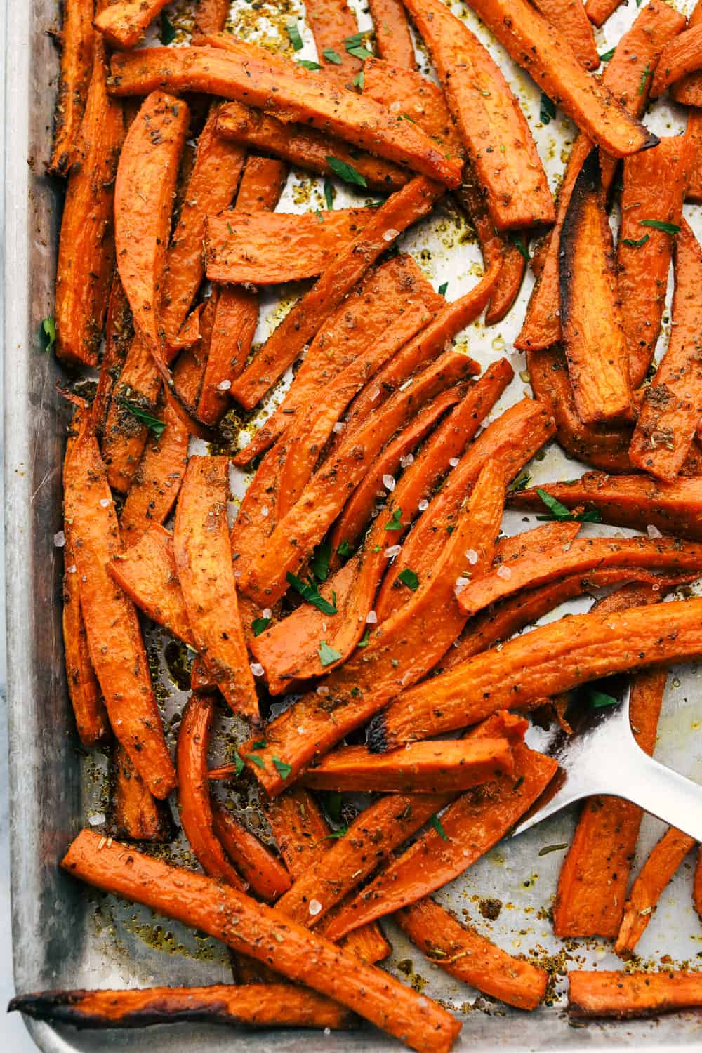 Crispy garlic sweet potato fries on a pan baked with a spatula scooping them out. 