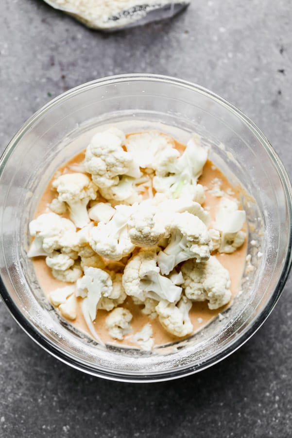 Cut up cauliflower in a bowl of buffalo sauce.