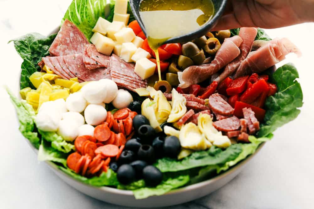 Antipasto salad with the lemon olive oil dressing being poured over top. 