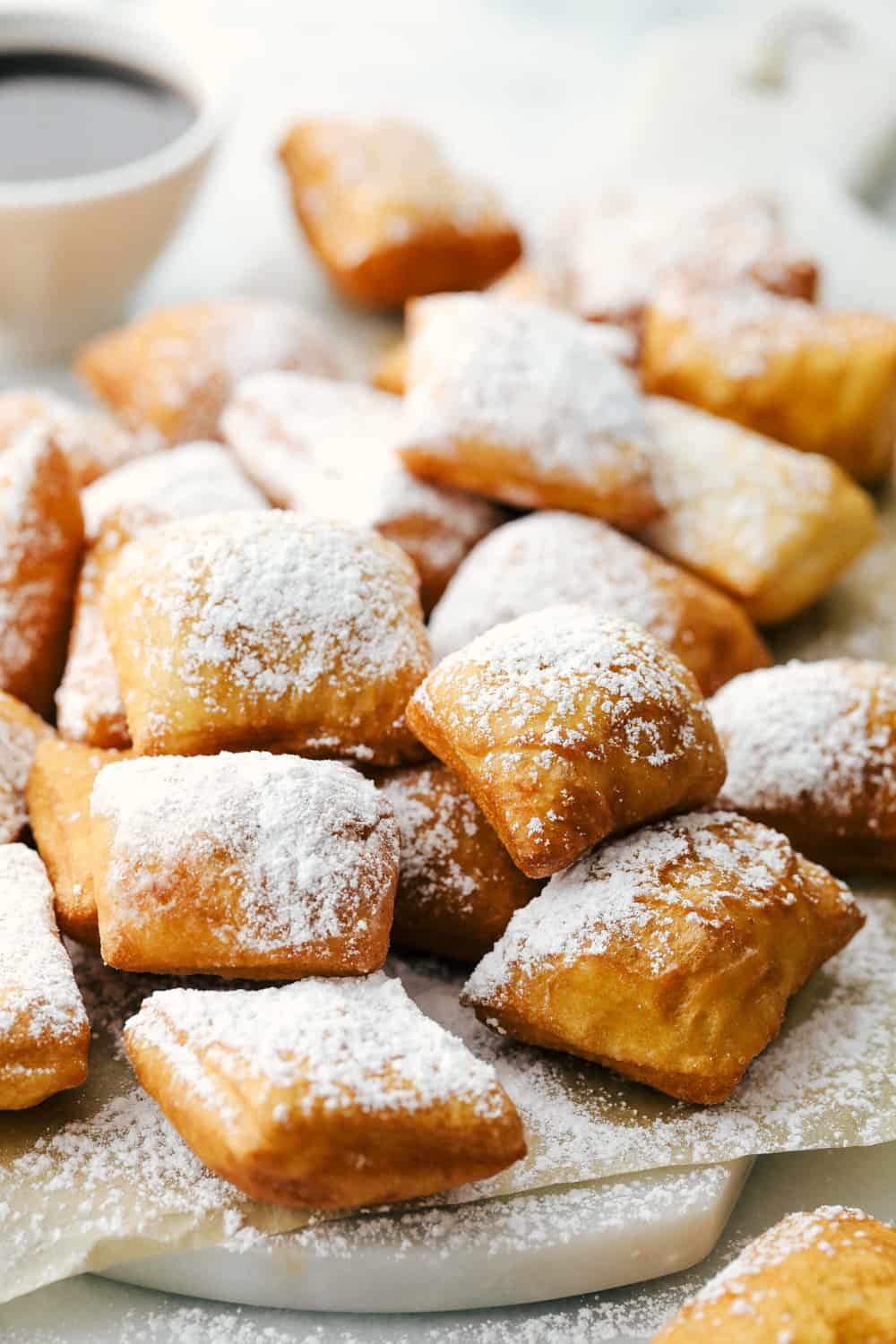 Several beignets on a cutting board sprinkled with powder sugar and chocolate syrup on the side. 