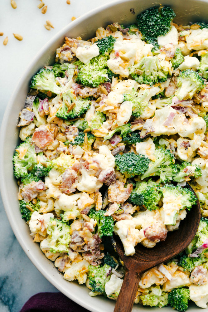 Cauliflower broccoli salad mixed together in a bowl with a wooden spoon.