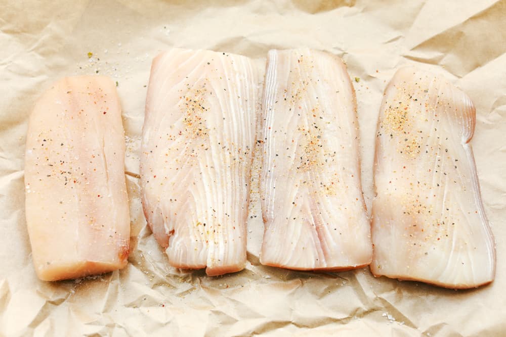 A row of four Mahi Mahi filets seasoned with salt and pepper. 