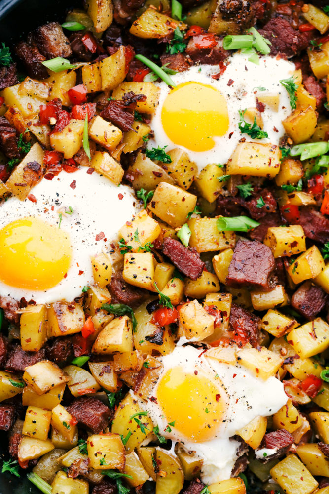 Corned beef with potatoes, corned beef and red bell peppers with eggs cooked on top.