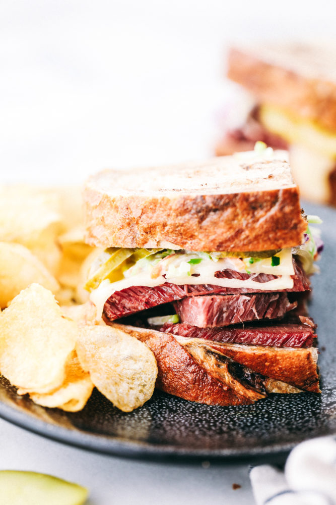 Corned beef sandwich on a plate with potato chips on the side. 