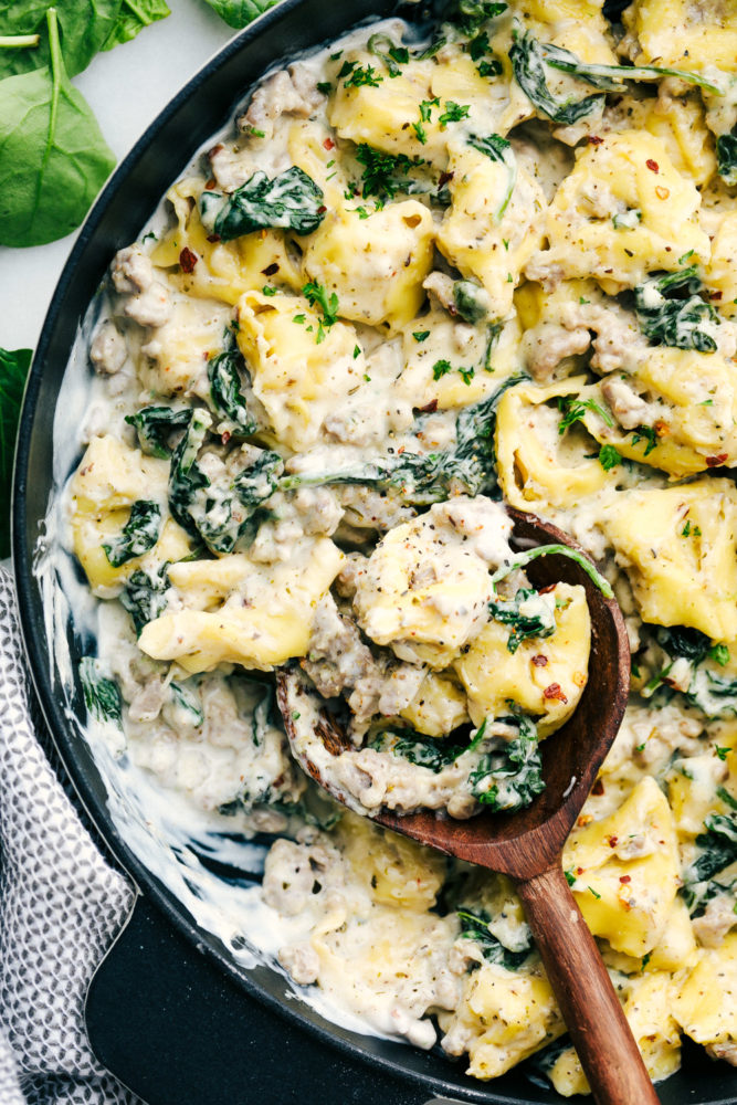 Creamy sausage tortellini skillet cooked together in a skillet with a wooden spoon stirred through. 