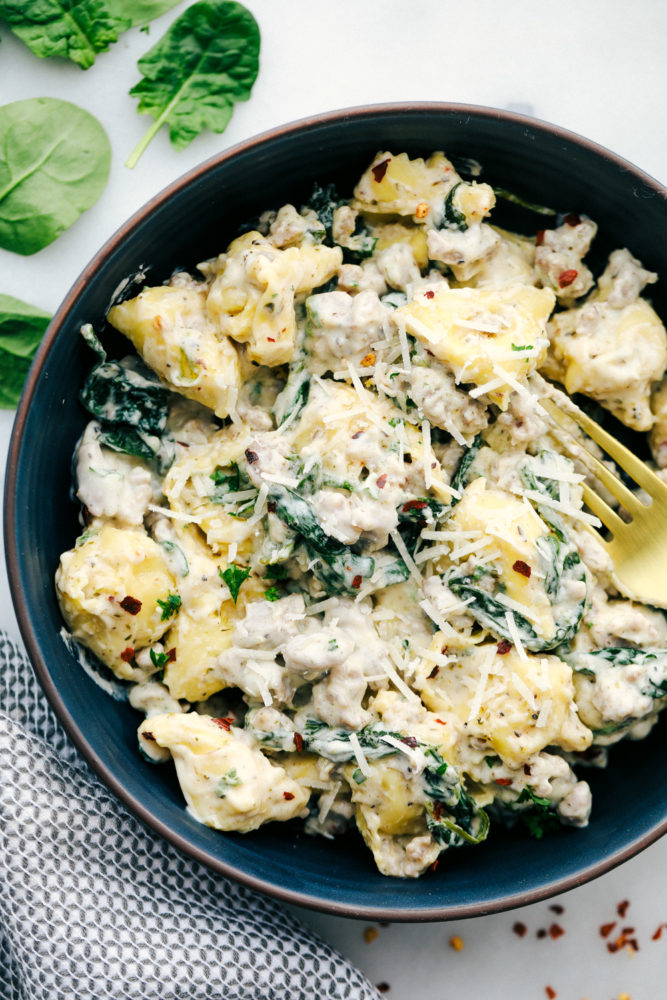 Sausage tortellini in a bowl with a fork and garnished with shredded parmesan. 