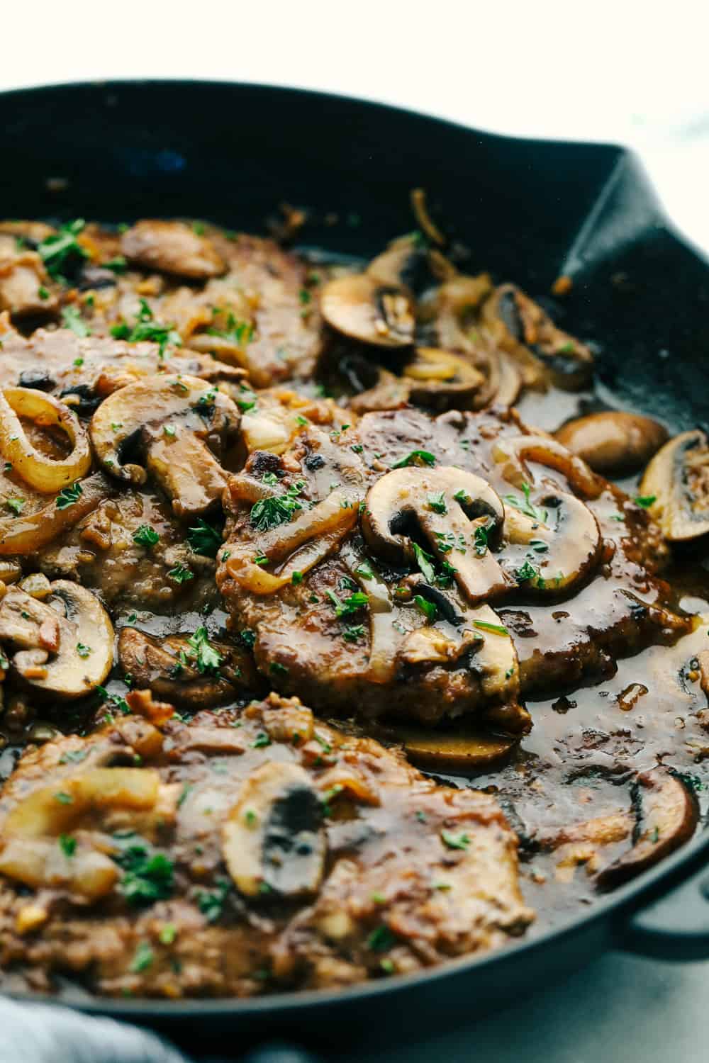 Cube steak in the mushroom gravy sauce cooking in a skillet.