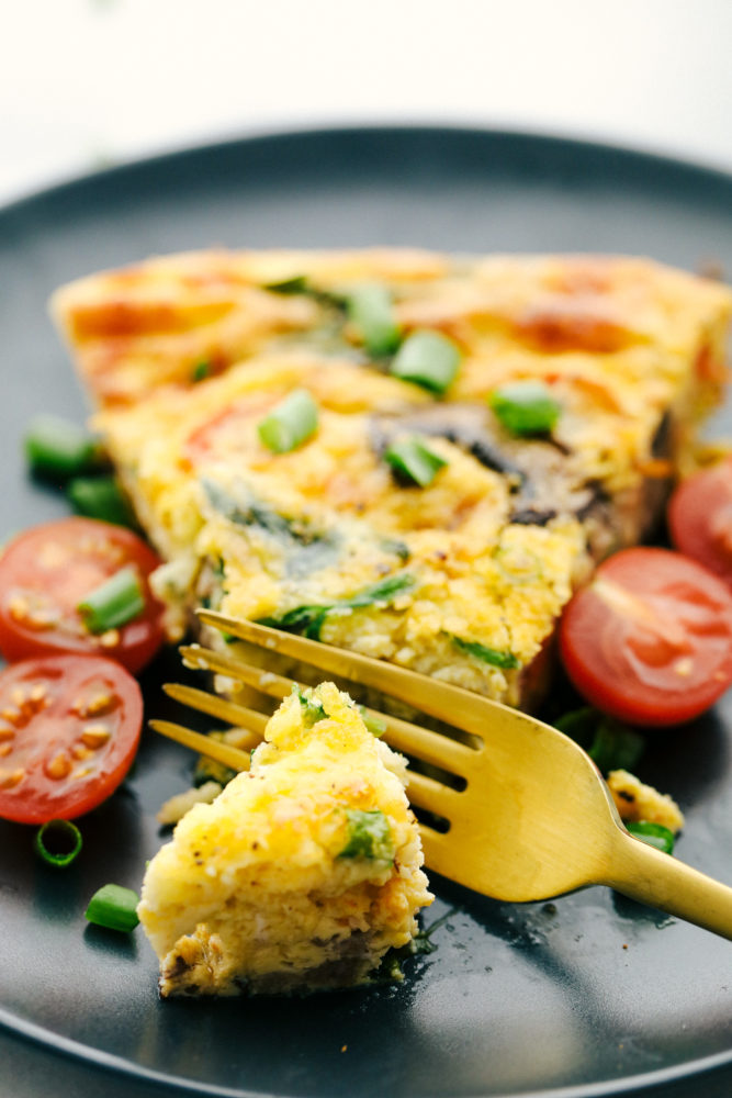 Sausage and mushroom frittata on a plate with a piece cut off with sliced cherry tomatoes on the side. 