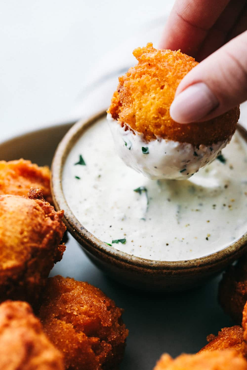 Hush puppies being dipped in tartar sauce. 