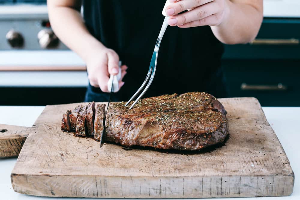 London Broil placed on a wooden cutting board being sliced in pieces with a knife. 