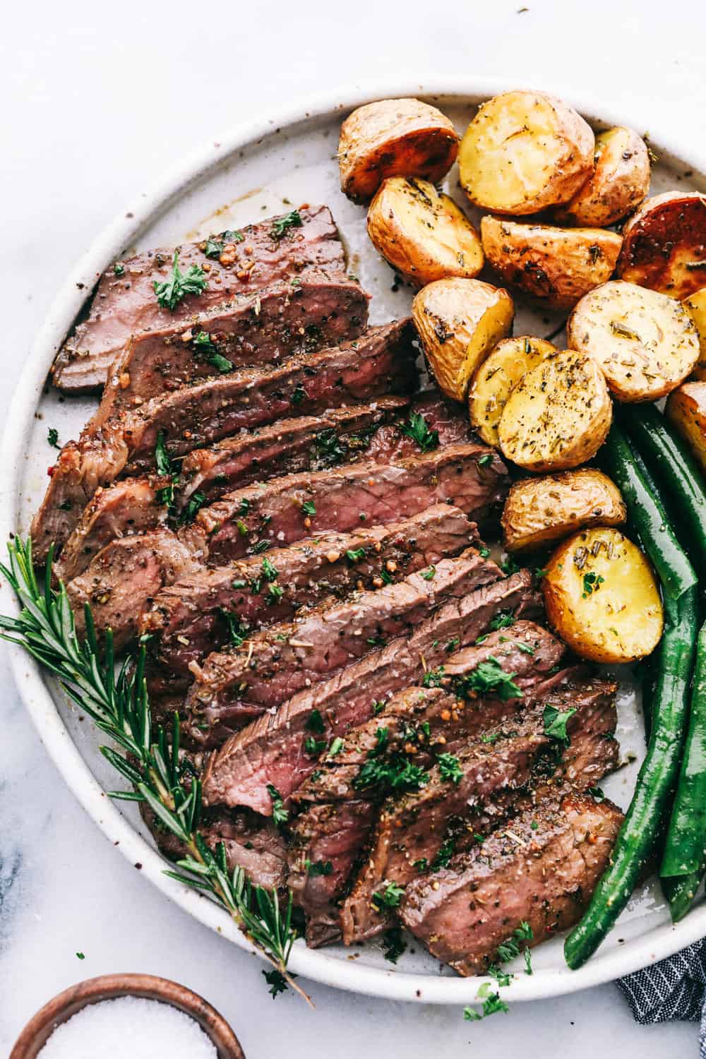 London Broil sliced on a plate with roasted potatoes and green beans. 