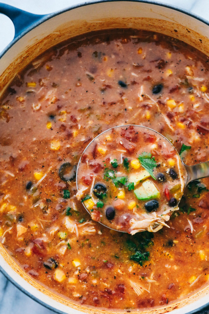 All 8 cans of ingredients in the taco chicken soup cooking in a pot with a ladle showing the ingredients cooking together. 