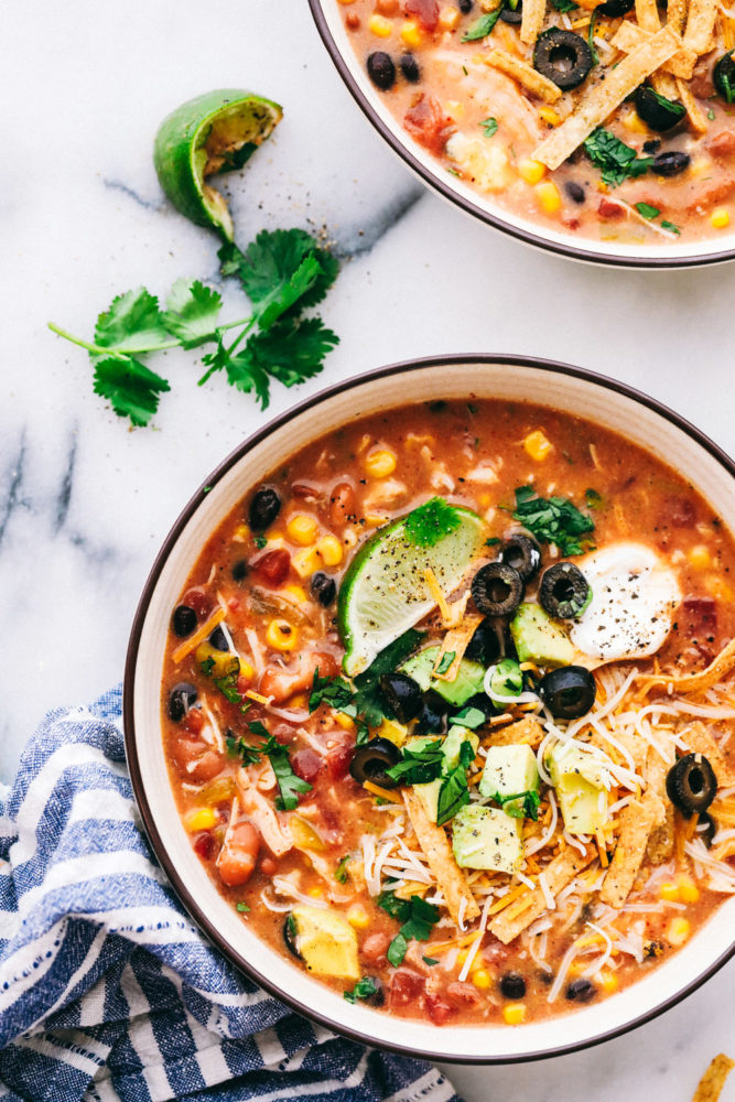 Two bowls of chicken taco soup garnished with sliced olives, limes and a dollop of sour cream. 