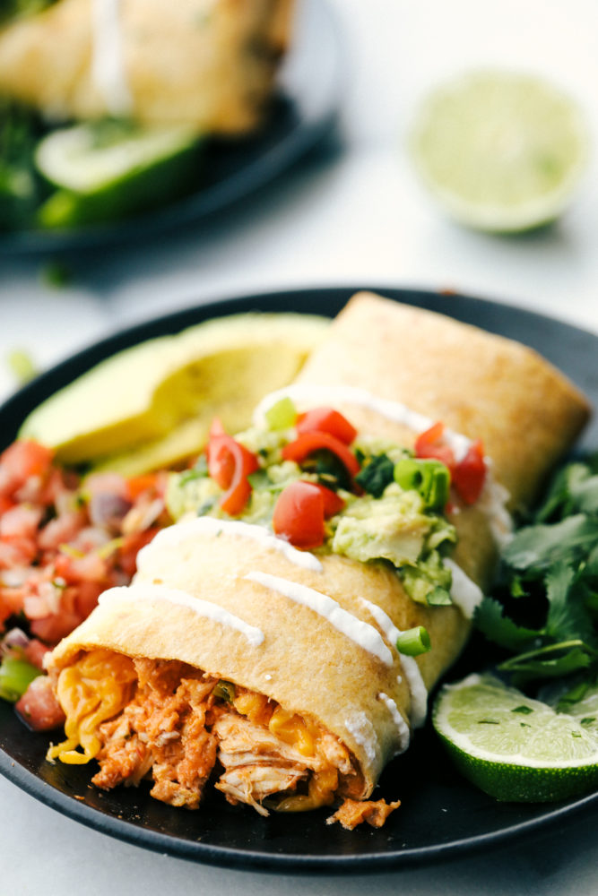 Chicken chimichanga on a plate with salsa, avocado and limes. 