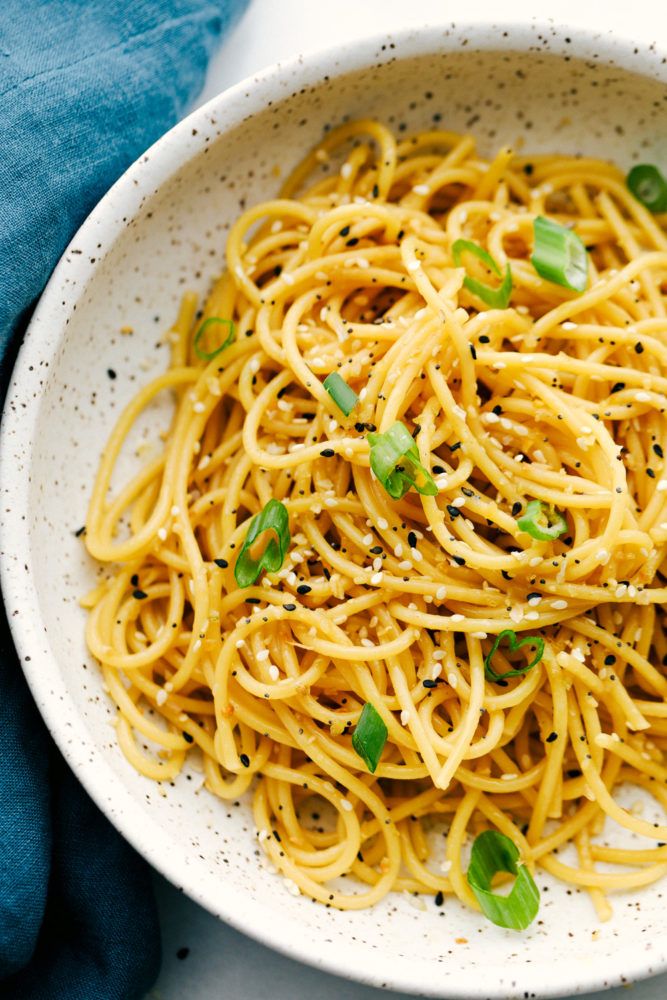 Garlic sesame noodles in a bowl garnished with green onions. 