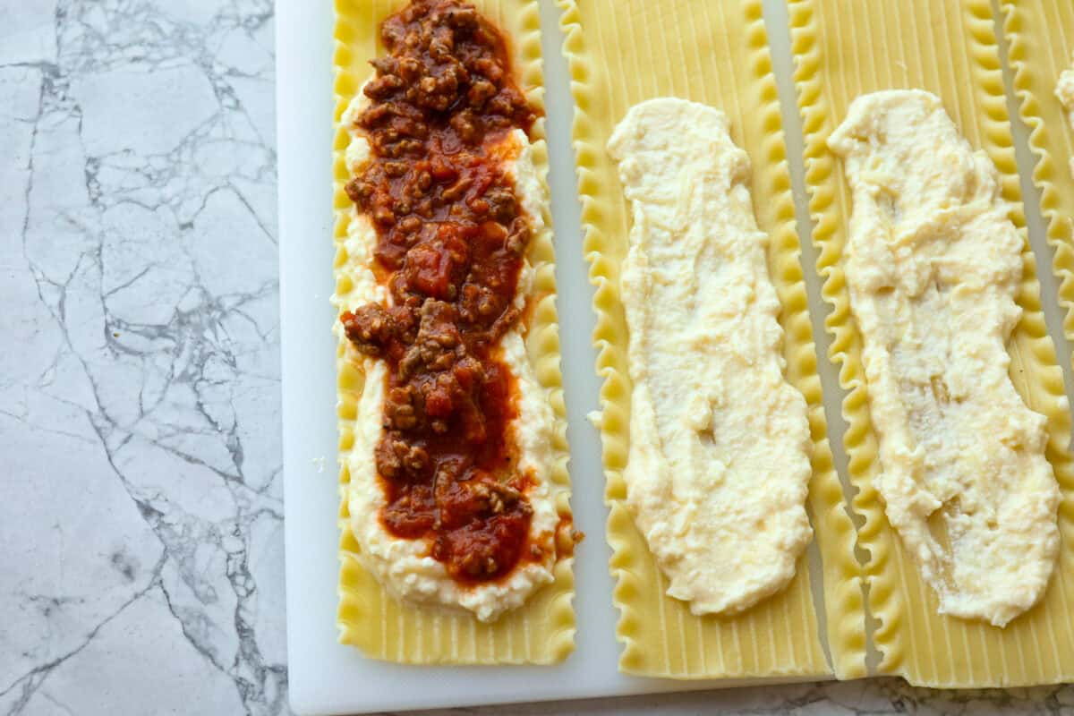 Overhead shot of meat and sauce mixture spread over cheese on individual lasagna noodles. 