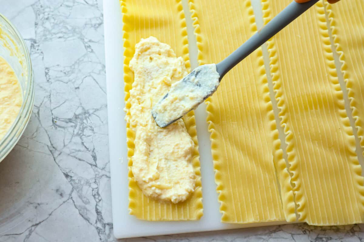 Overhead shot of cheese mixture being spread on individual lasagna noodles. 