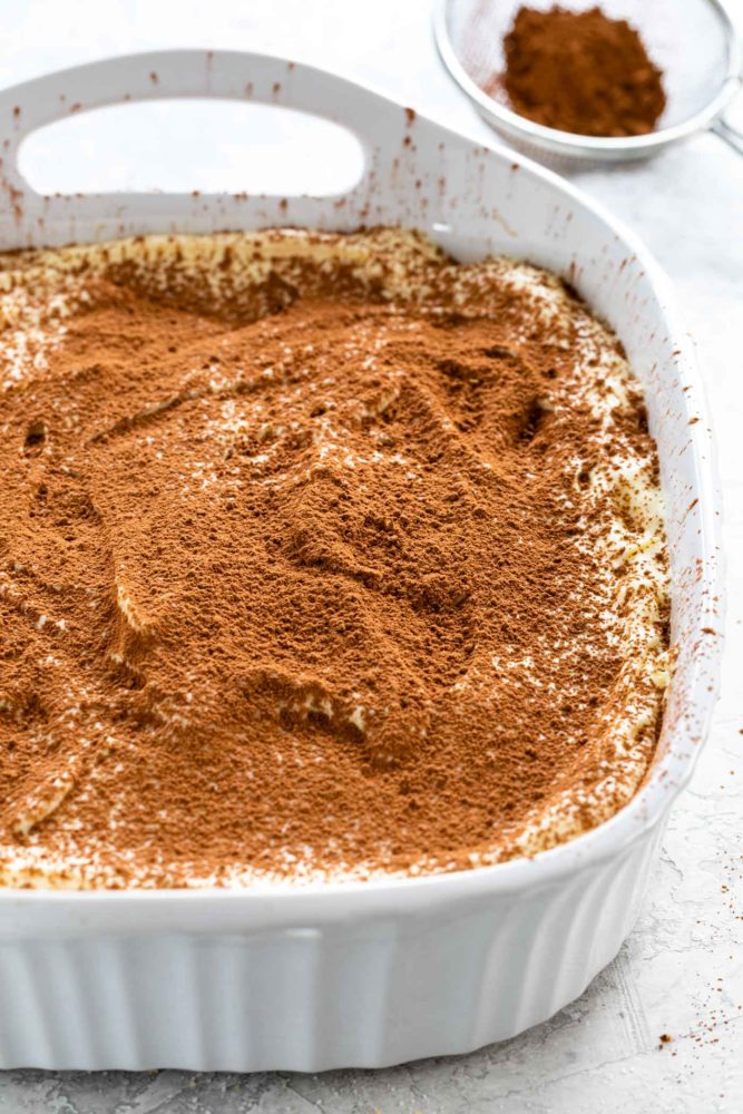 sprinkling cocoa powder over tiramisu