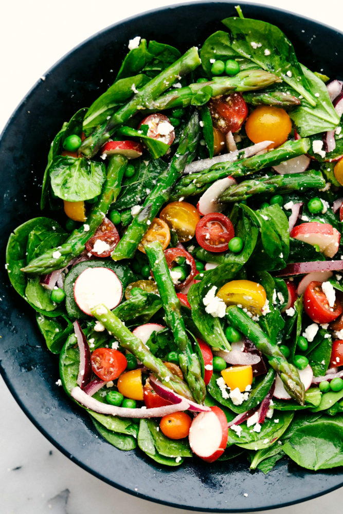 Asparagus salad with tomatoes, radish and spinach in a black bowl. 