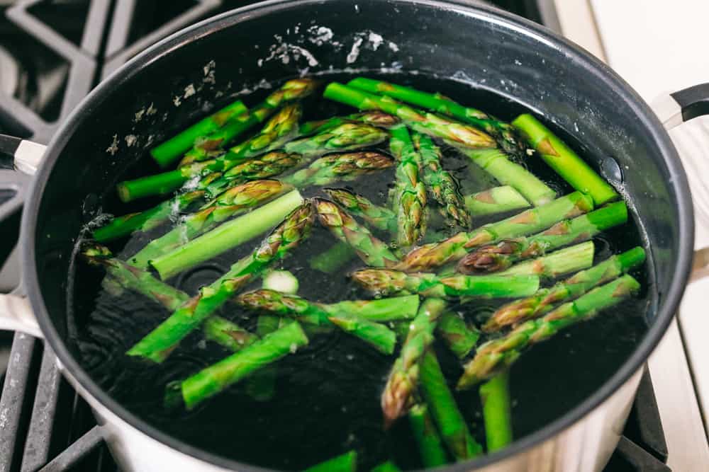 Asparagus cooking in boiling water on a gas stove top. 