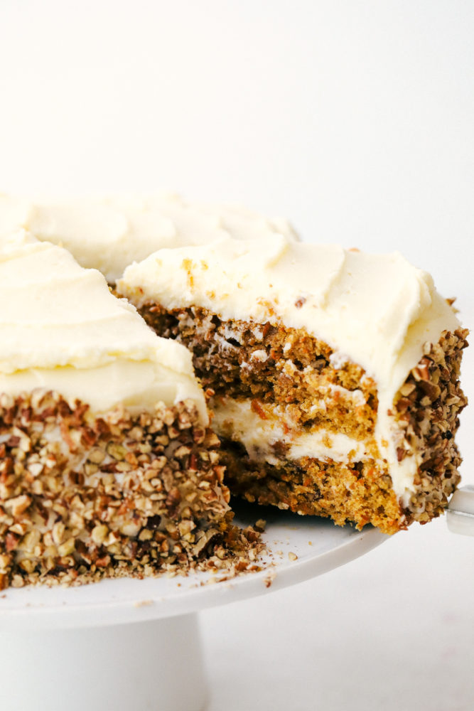 Carrot cake sliced and being pulled away from the cake platter. 