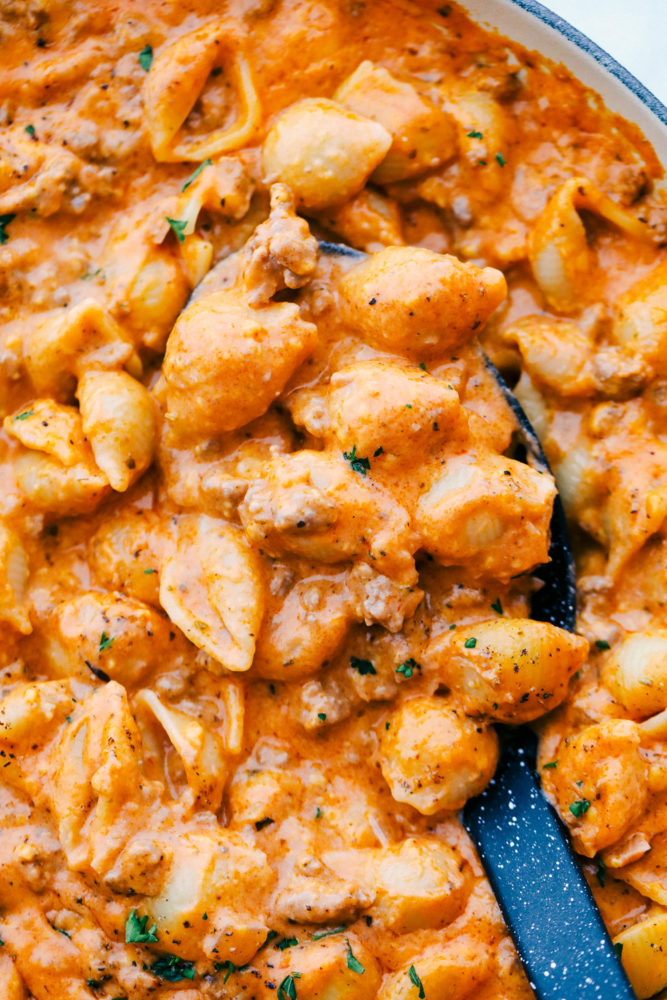 Cheesy beef and shells in a skillet with a ladle stirring them up. 