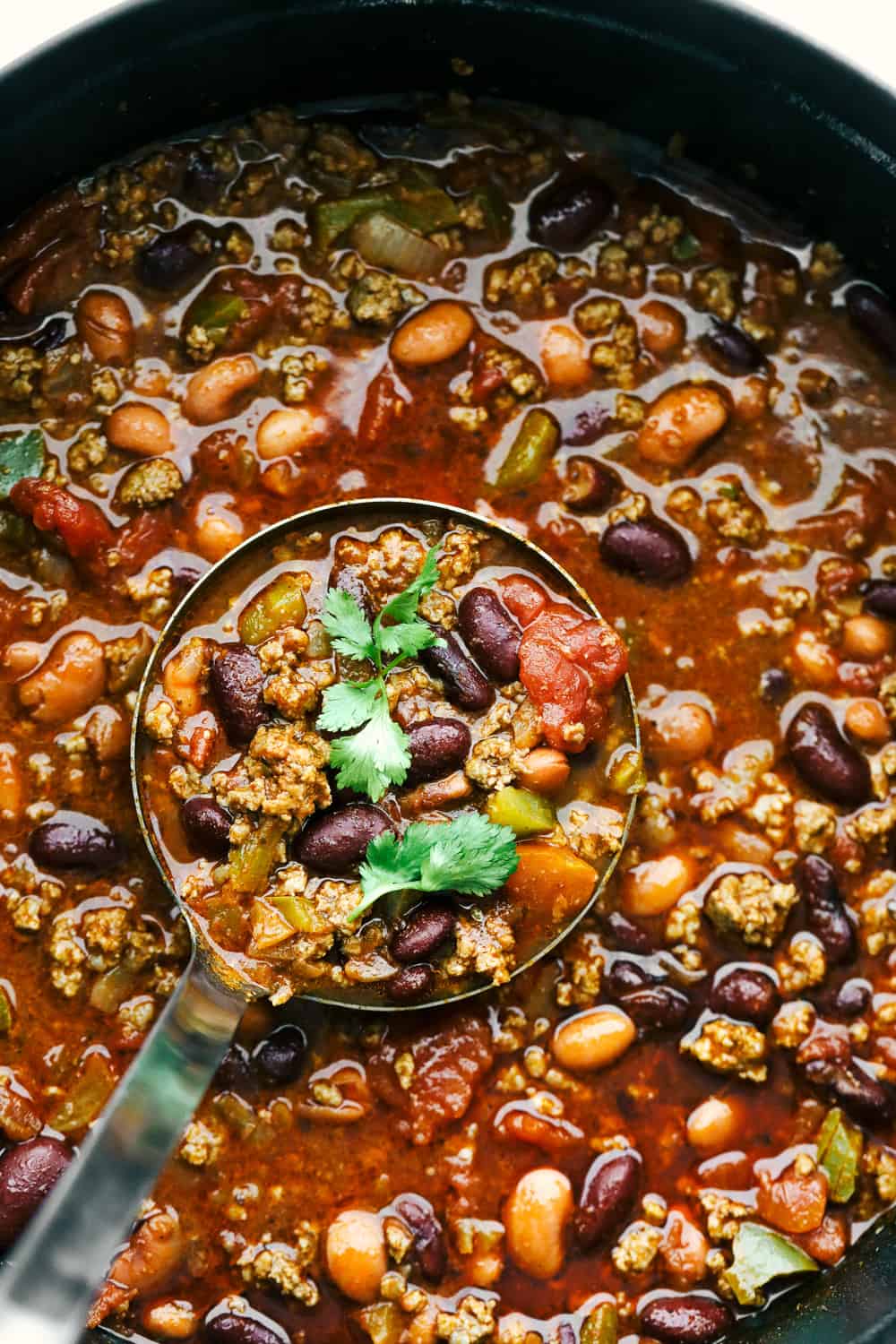 Chili in a large pot with a ladle spooning out a spoonful of chili for the camera. 