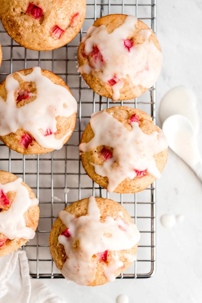 Glazed Rhubarb Muffins on a wire rack with a spoonful of glaze to the side.