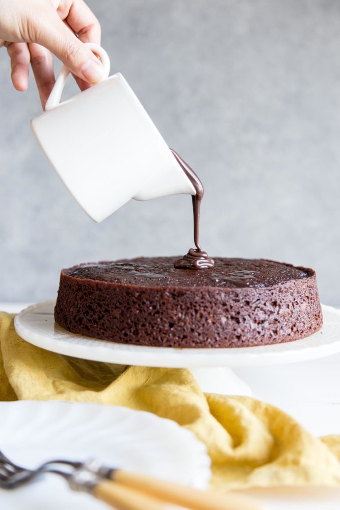 Pouring chocolate ganache on top of a chocolate cake