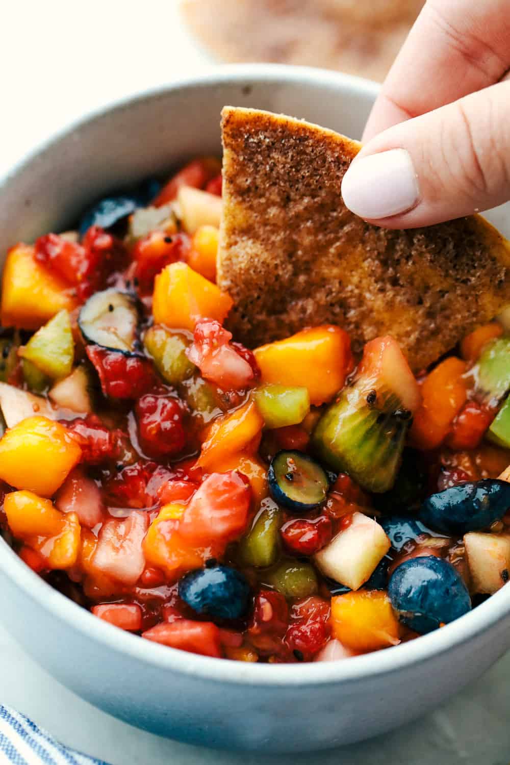 Fruit salsa in a bowl with a cinnamon chip being dipped in it. 