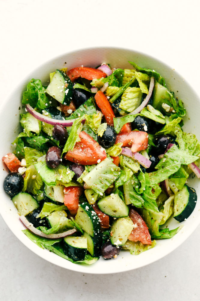 Greek Salad Dressing poured over a Greek Salad in a white bowl. 