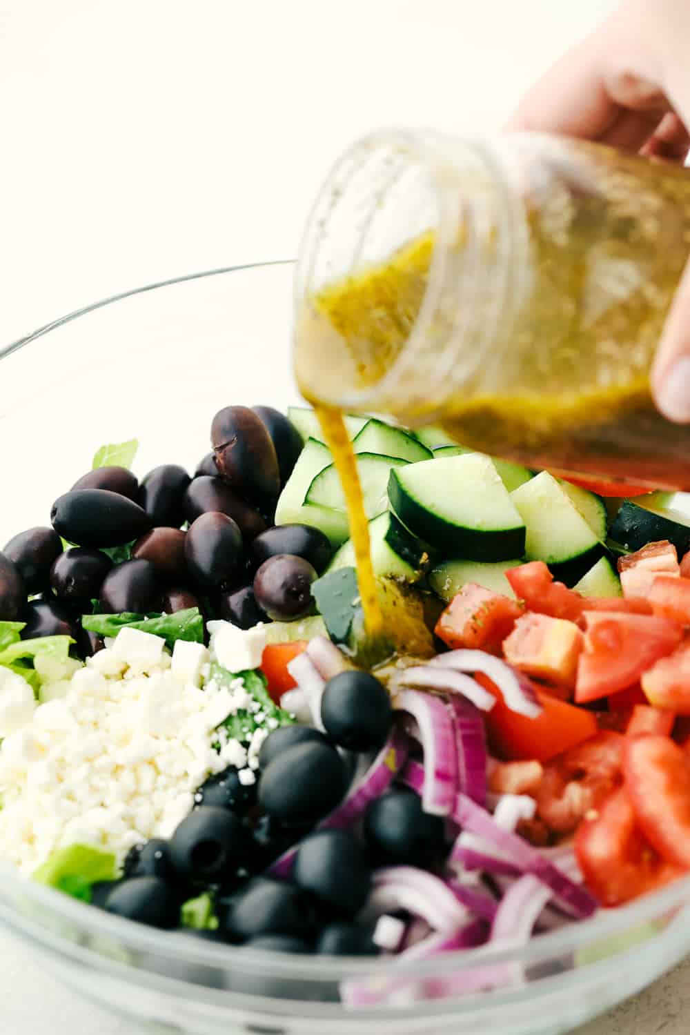 Pouring dressing on Greek salad ingredients.