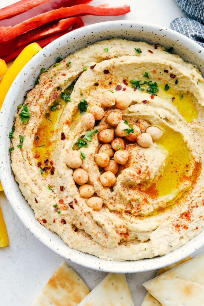 Hummus in a white speckled bowl with chickpeas garnished over top. 