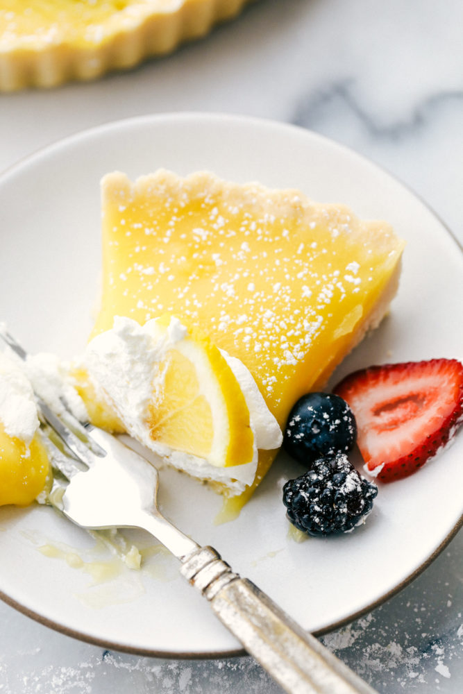 Lemon tart on a white plate with fresh berries on the side and a bite taken out of the tart.