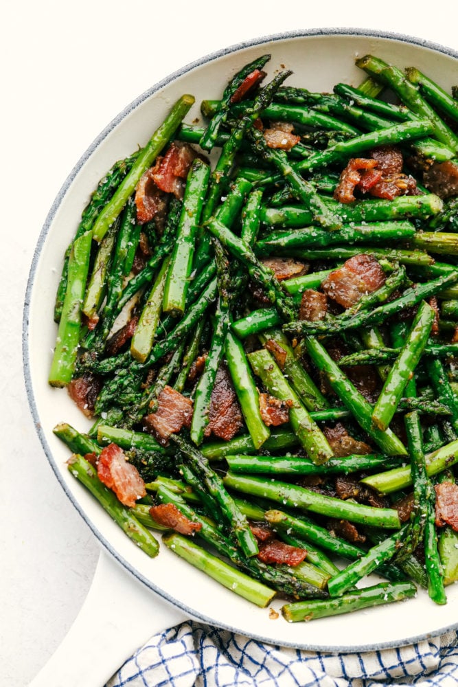 Garlic asparagus with bacon in a white skillet.