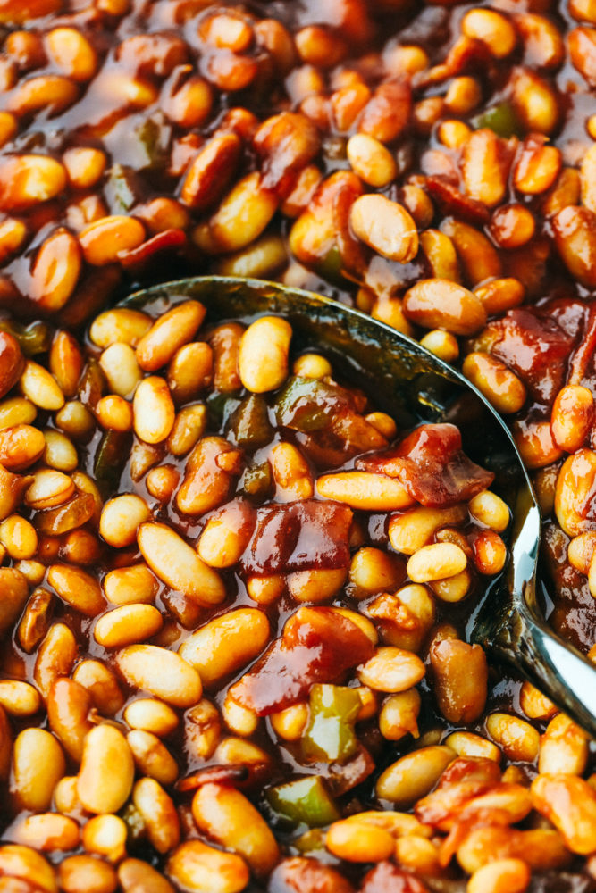 Close up on finished baked beans being scooped with a serving spoon.