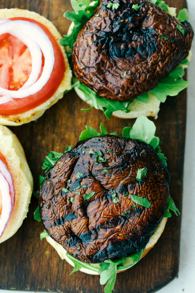 Layering portobello mushrooms in a hamburger bun with tomato, arugala, and onion.