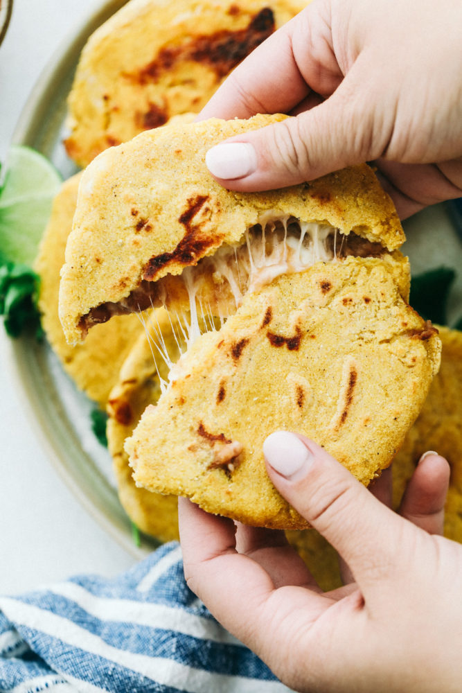 Easy Bean and Cheese Pupusas being ripped into two pieces to reveal gooey cheese inside.