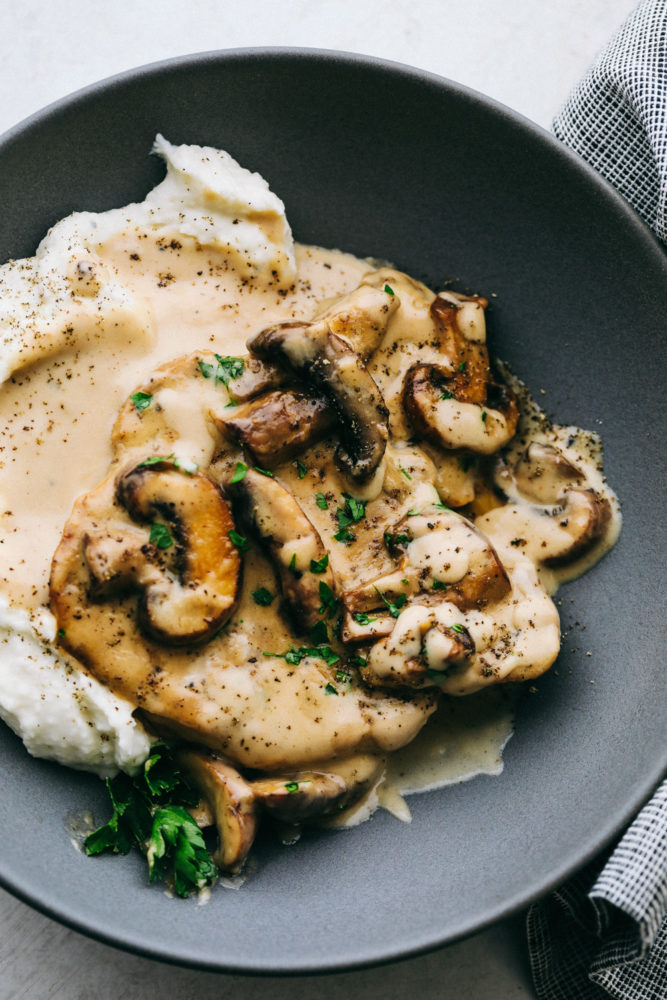 Smothered pork chops plated with mashed potatoes on a black plate.