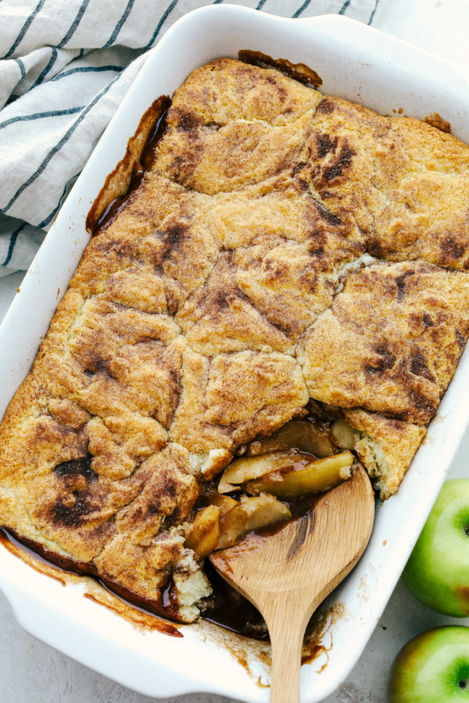 Scooping apple cobbler out of a white dish.