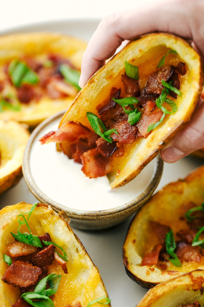 A potato skin being dipped in ranch sauce. 