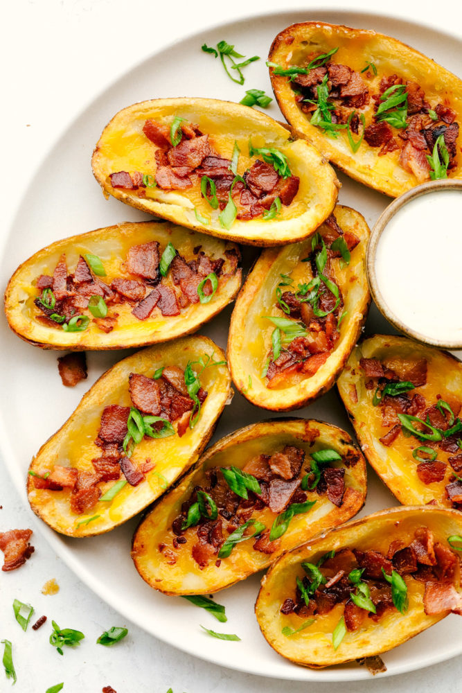 Potato skins on a white plate with ranch dipping sauce on the side. 